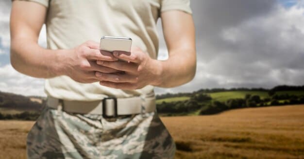A soldier using a high-tech communication device in a field environment, with a focus on the device's interface and the soldier's focused expression. The background shows a blurred scene of tents and other soldiers.