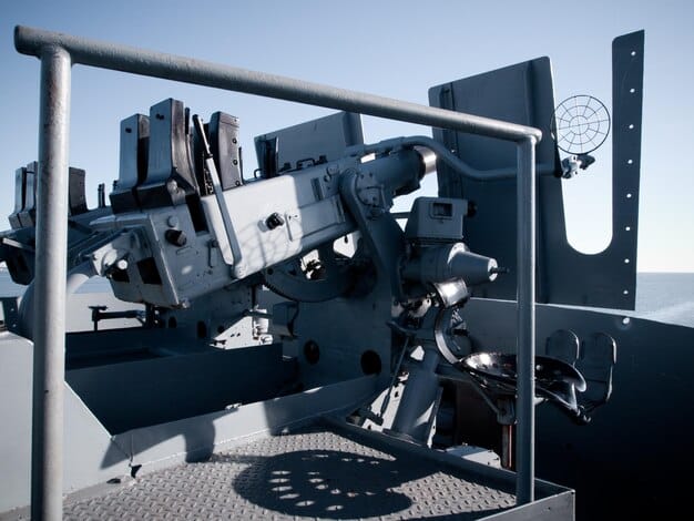 A close-up view of the Laser Weapon System (LaWS) mounted on the deck of a US Navy ship, with detailed visible components of the laser emitter and targeting array, set against a calm ocean backdrop.