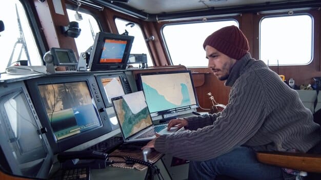 A naval technician monitoring data from multiple screens displaying real-time sonar readings and navigation maps from an autonomous underwater vehicle (AUV) during a simulation.